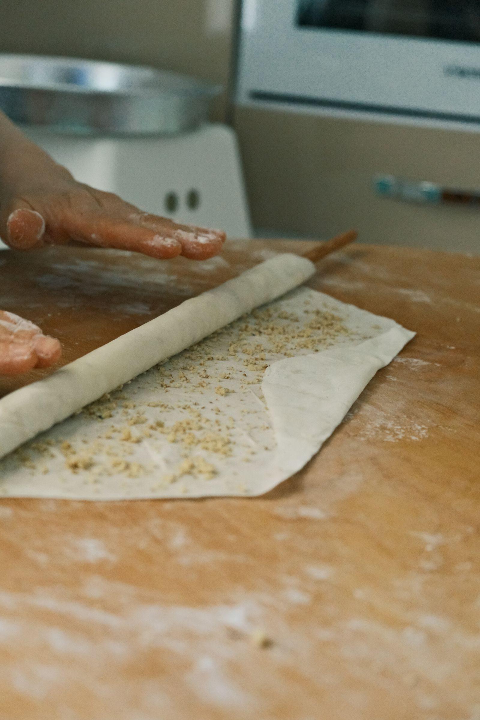 Flour-dusted hands rolling out dough on a wooden work surface.