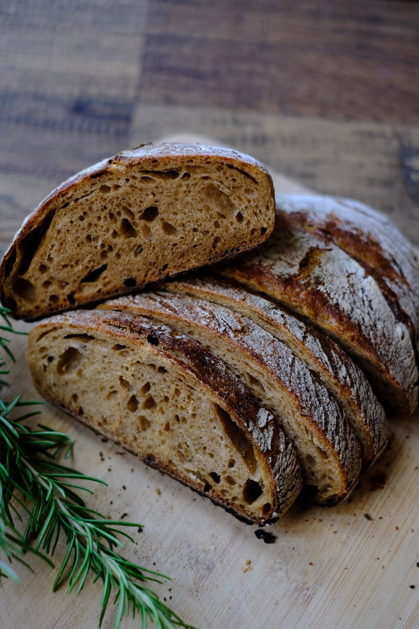 A deeply scored, crusty sourdough loaf cooling on a wooden board, dusted with flour.